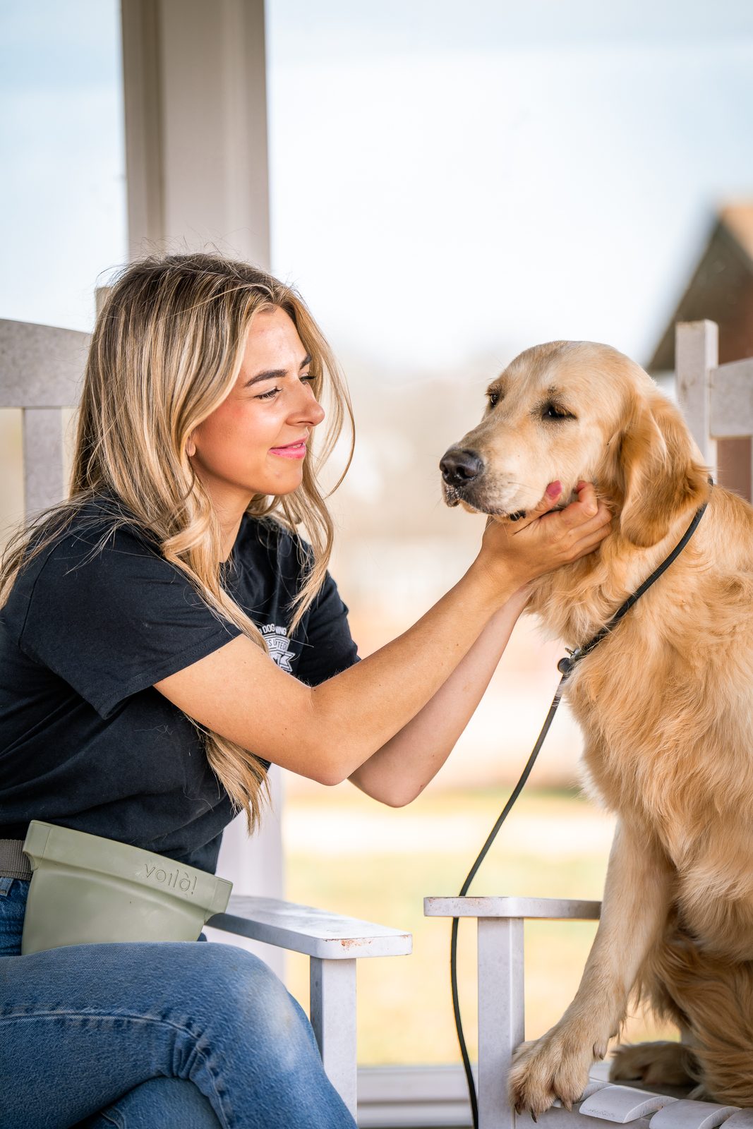 A woman petting the face of a golden retriever on a sunny porch